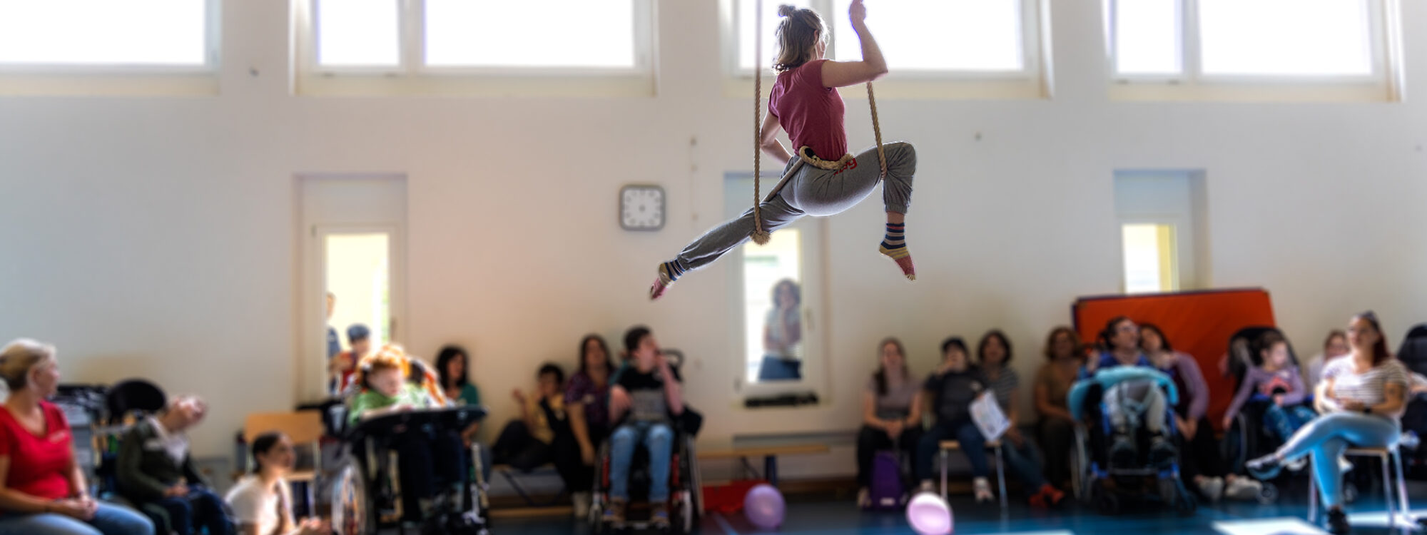 Eine Frau schwebt vor einer Klasse von Kindern und Erwachsenen in der Luft. Sie alle sind in der Trunhalle.